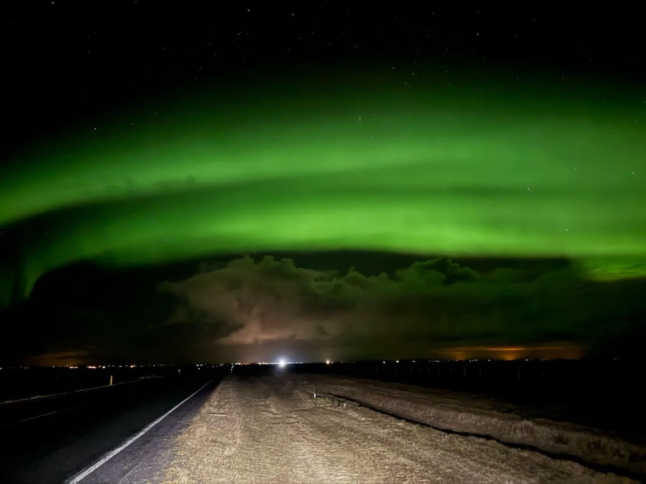 A green aurora arc stretching across the sky above an empty road outside Reykjavik