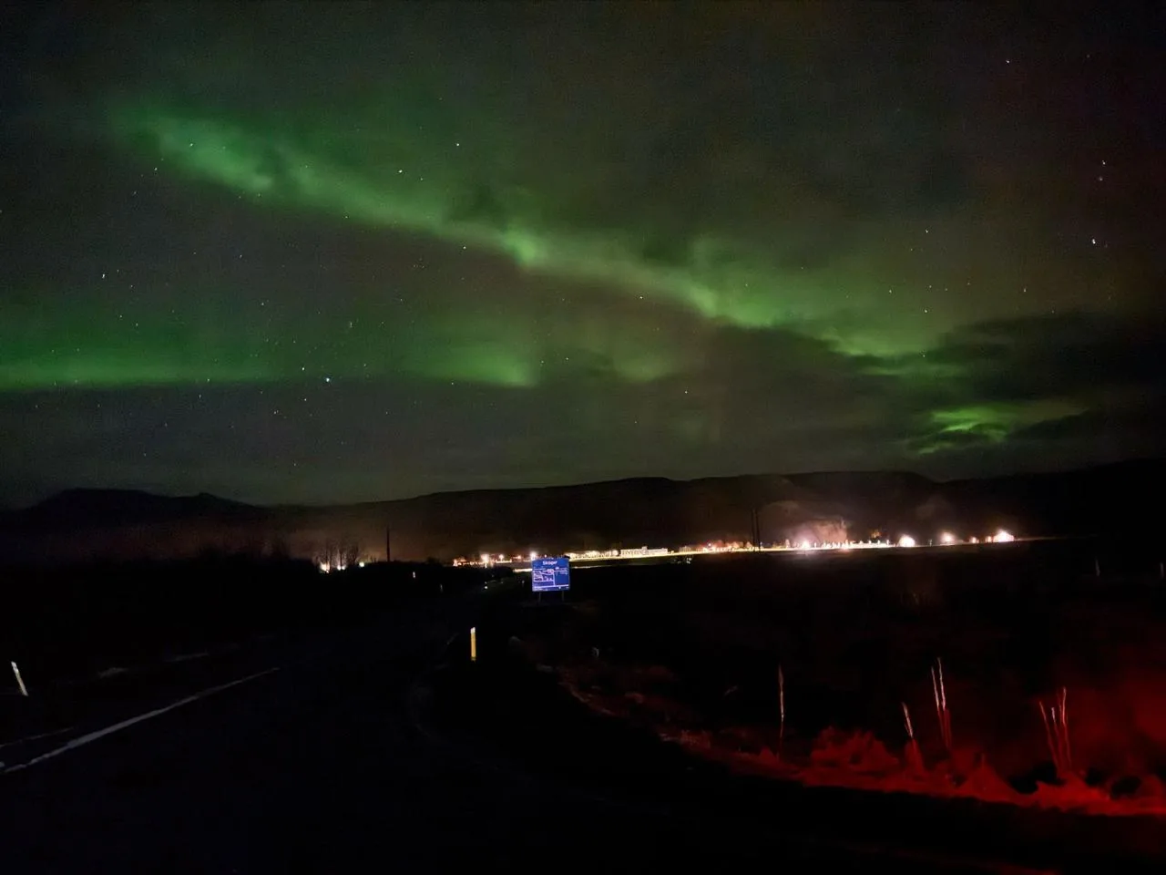 Northern lights above the road out of Reykjavik, with the last town lights on the horizon